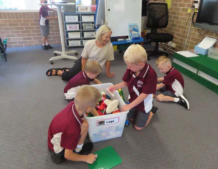A teacher sitting on the floor with three students looking through a box of resources.